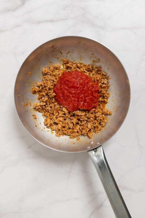 Cooked ground beef with tomato sauce in a stainless steel skillet.