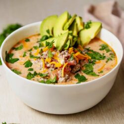 Creamy chicken tortilla soup with avocado, cheese, and fresh herbs in a white bowl.