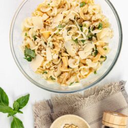 Creamy three-cheese pasta salad with basil and pine nuts in a glass bowl.