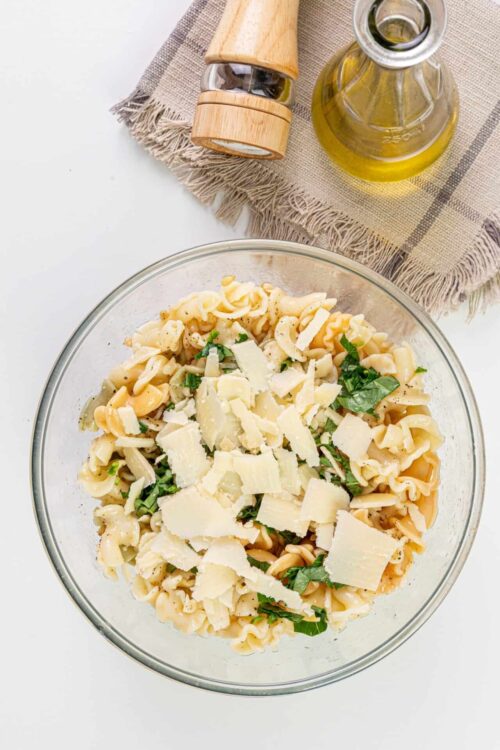 Creamy pasta salad with cheese, herbs, and a tangy dressing in a glass bowl.
