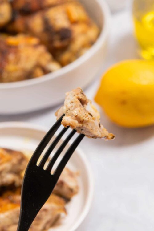Creamy chicken and mushroom casserole on a fork, served with fresh lemon slices, baked in a white dish, comforting homemade dinner.