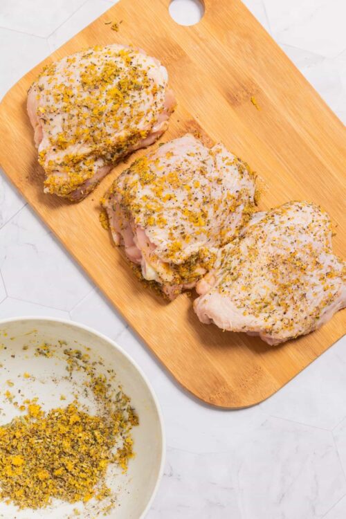 Bolstered oven-ready chicken thighs with lemon herb seasoning on a wooden cutting board.