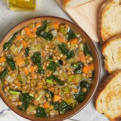 Creamy lentil vegetable soup with fresh bread on a rustic table, healthy and hearty meal option.