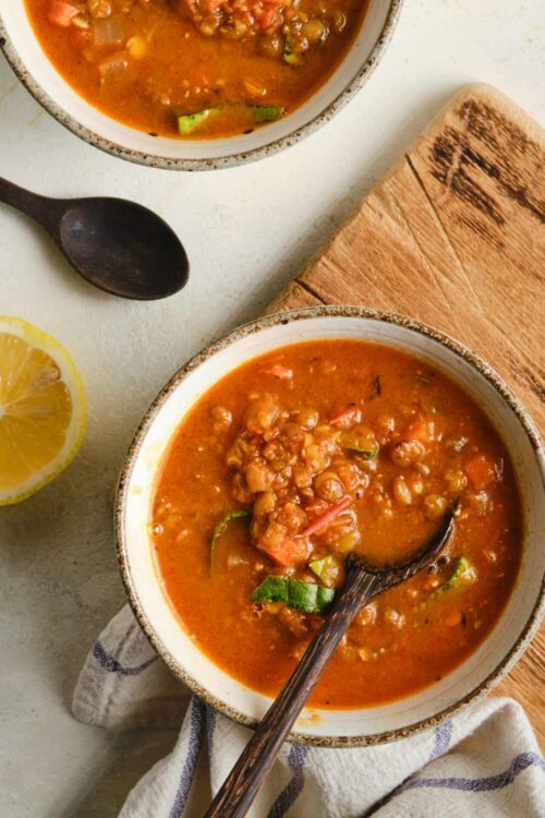 Savory lentil soup with vegetables in a rustic bowl, served with lemon wedge.
