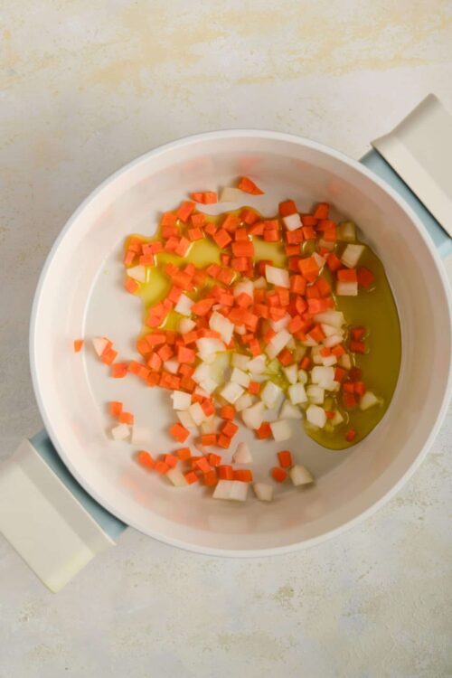 Diced carrots and onions in a slow cooker with cooking oil.