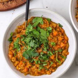 Creamy vegetable lentil stew garnished with fresh herbs in a white bowl.