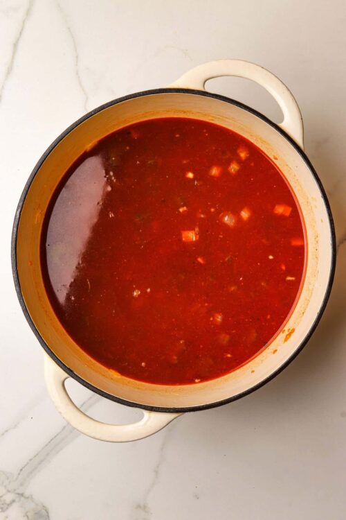 Rich tomato soup simmering in a white enameled pot on a marble countertop.