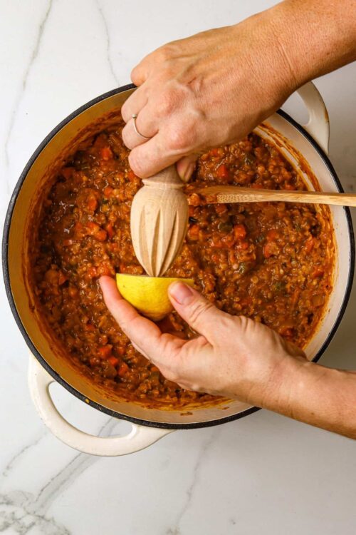 Savory homemade lentil stew being prepared in a pot with lemon, wooden spoons, and stirring utensils for comforting kitchen recipe.