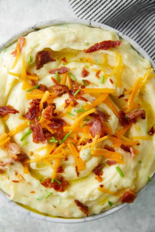 Creamy loaded mashed potatoes with cheese, bacon, and chives in a bowl.