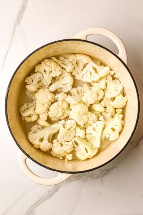 Chopped cauliflower in a yellow enamel-coated cast iron pot ready for roasting.