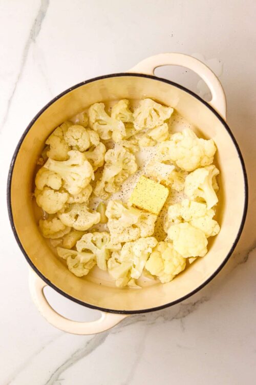 Cream cauliflower florets in a cream sauce with butter in a yellow ceramic baking dish.