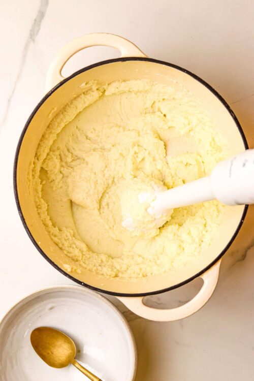 Fluffy homemade potato mashed potatoes in a cast iron pot with an immersion blender.