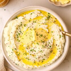 Creamy mashed potatoes with butter, chives, and black pepper in a white bowl.