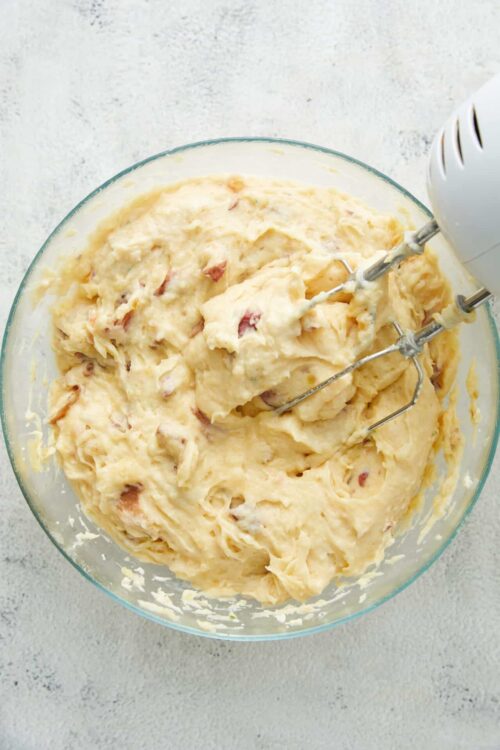Creamy potato salad with bacon bits and mayonnaise in a glass mixing bowl. Hand mixer mixing ingredients. Fresh homemade potato salad.