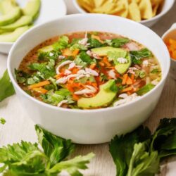 Fresh chicken tortilla soup with avocado, cilantro, and shredded chicken in a white bowl.