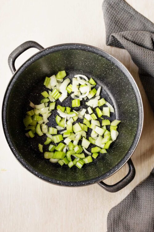 Chopped celery cooking in a non-stick skillet for recipe preparation.