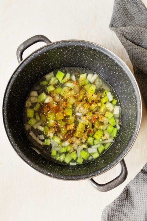 Sautéed green onions in a black skillet with seasoning and spices.