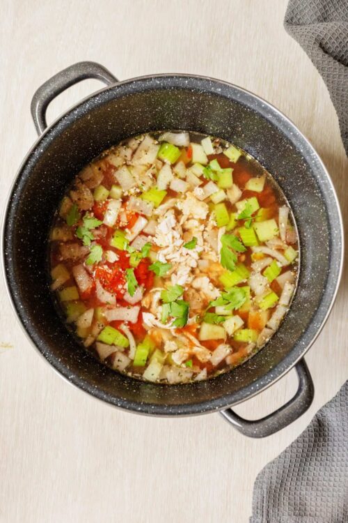 Simmering chicken soup with vegetables in a black pot.