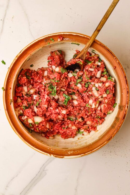 Shredded beef taco meat in a rustic bowl with fresh herbs and onions.