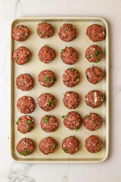 Seasoned beef meatballs on baking sheet with chopped herbs, ready to bake, homemade meatball recipe.