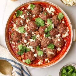 Juicy homemade meatballs in tomato sauce garnished with fresh cilantro and crumbled cheese. Perfect comfort food recipe from Baked Bree.