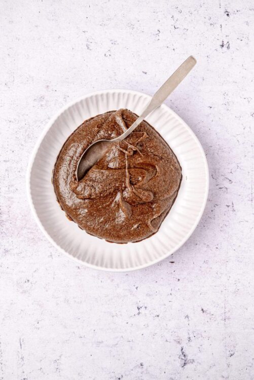 Decadent chocolate mousse in a white bowl with a silver spoon, perfect for dessert.