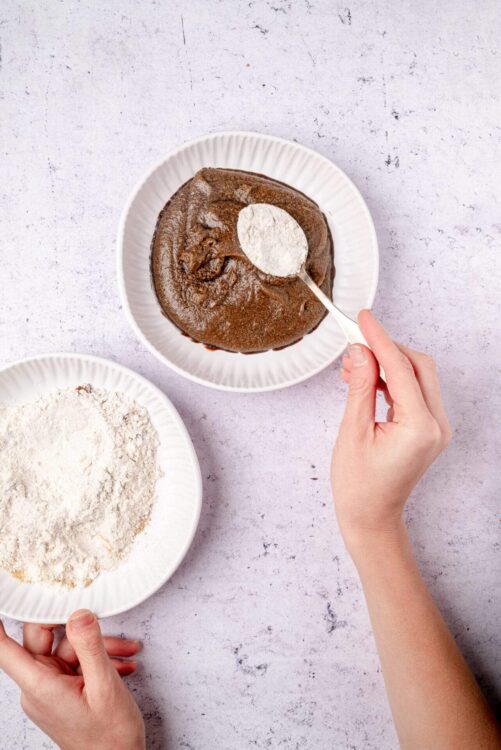 Rich chocolate cake with flour for baking on white plate.