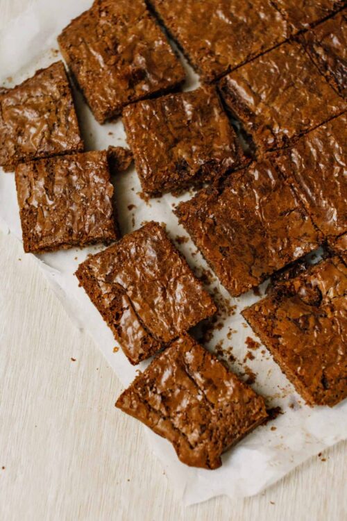 Fudgy chocolate brownies with cracked tops on parchment paper.