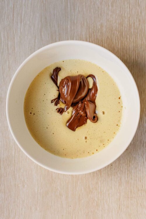 Creamy vanilla pudding with melted chocolate swirls, served in a white bowl on a light wooden surface.