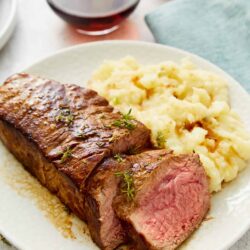 Juicy prime rib with mashed potatoes and rosemary garnish on a white plate.