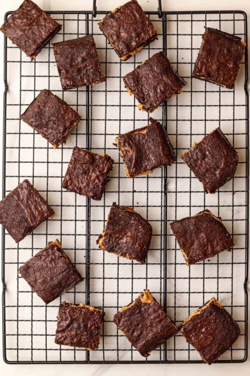 Rich chocolate brownies with crackly topping on cooling rack.
