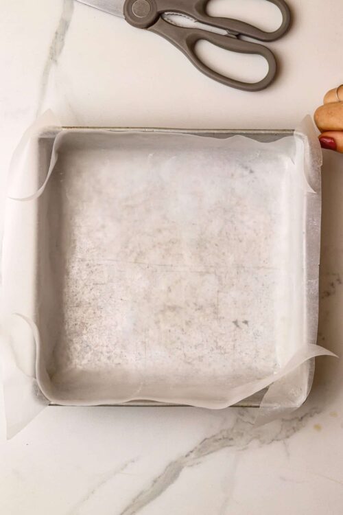 Butter paper lining a baking tray with gray scissors on white marble surface.