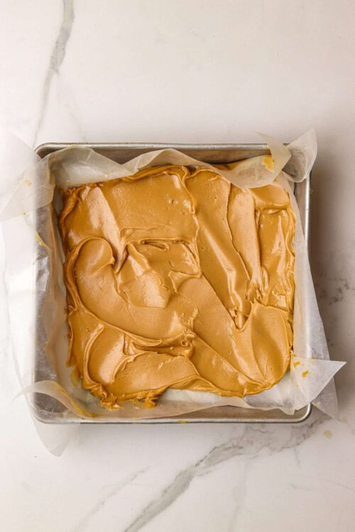 Creamy caramel frosting spread over a freshly baked cake in a baking pan.