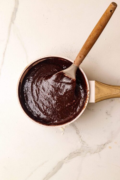 Rich chocolate sauce in a saucepan with a wooden spatula, perfect for baking recipes.