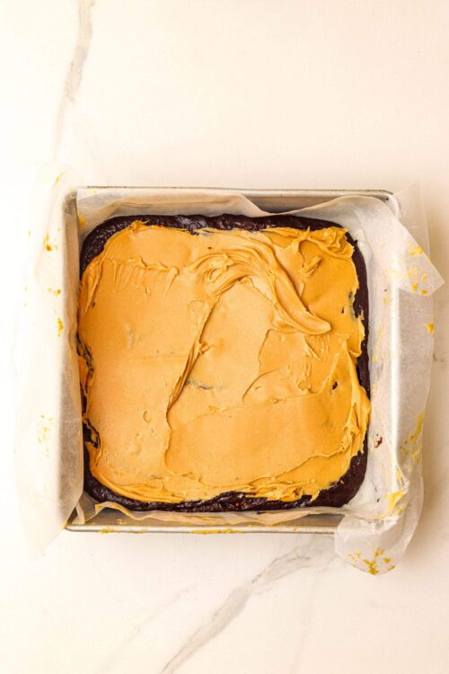 Creamy peanut butter frosting on a freshly baked brownie in a baking pan.