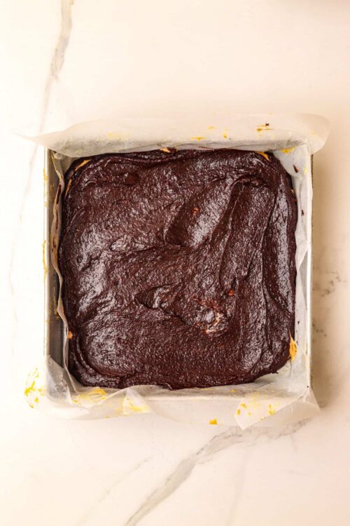 Rich chocolate brownie batter in a lined baking pan ready for baking.