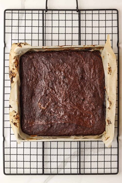 Fudgy homemade chocolate brownie baked in parchment-lined pan, cooling on a wire rack.