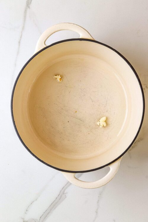 Empty enamel cast iron pot with some popcorn kernels inside on a marble countertop.
