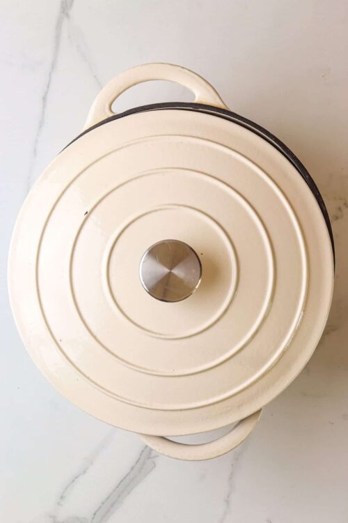 Cream-colored vintage cake dome with a metal handle on top, placed on a marble surface.