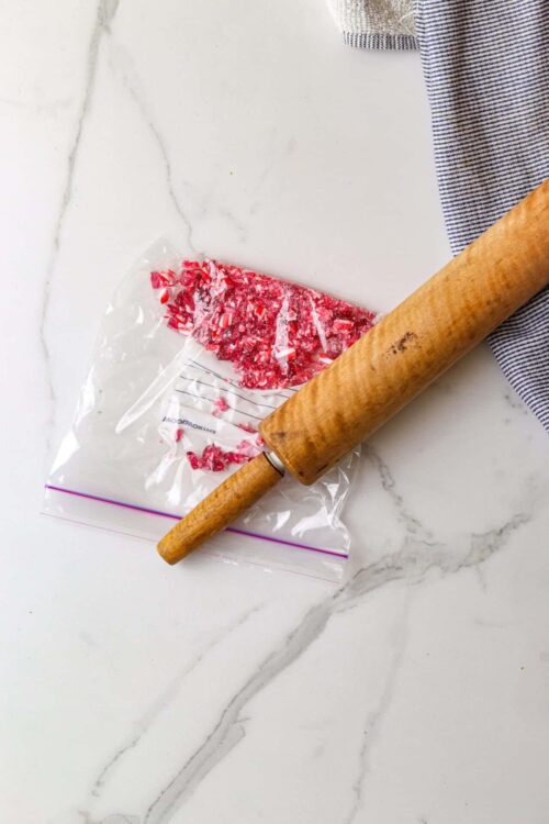 Crushed peppermint candy on a baking sheet with a rolling pin and striped cloth.