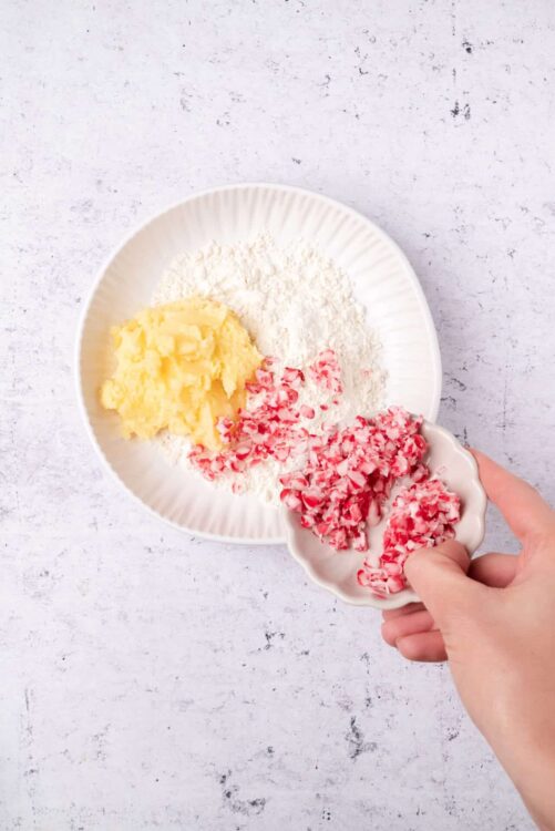 Buttery mashed potatoes, chopped peppermint candy, flour, and powdered sugar in a bowl.