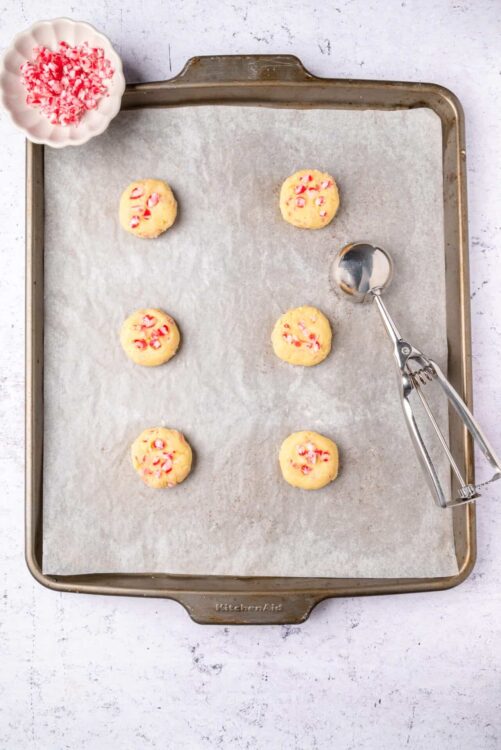 Buttery cookie dough balls with red and white candy cane pieces on a baking sheet.