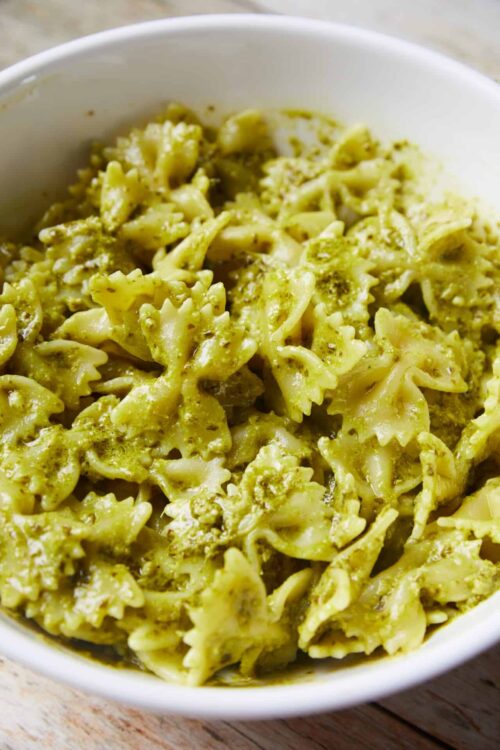 Creamy pesto pasta with bowtie and spiral-shaped noodles in a white bowl.