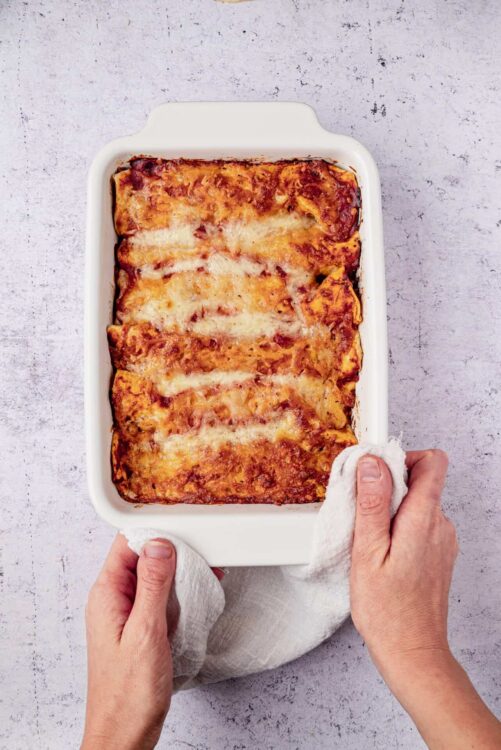 Golden baked lasagna with melted cheese in a white casserole dish on textured surface.