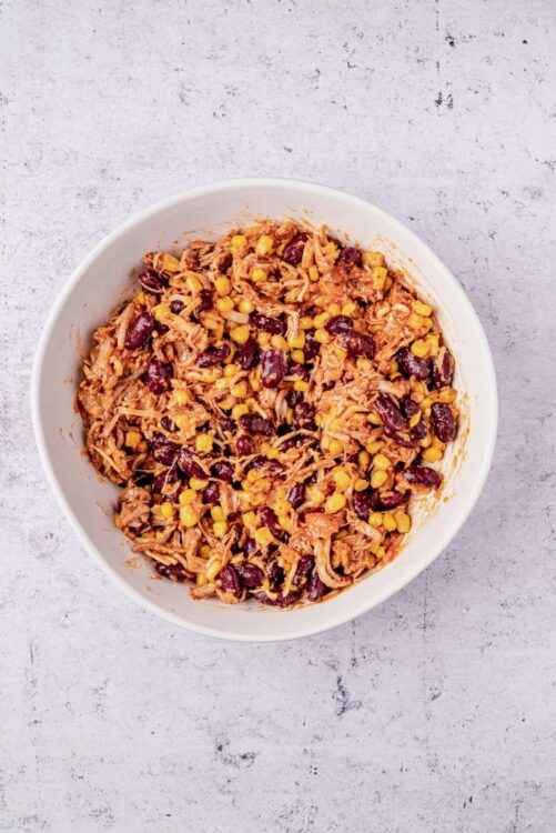 Savory pulled chicken and black bean chili in a white bowl, shredded chicken, corn, beans, and chili spices, easy comfort food recipe, Baked Bree.