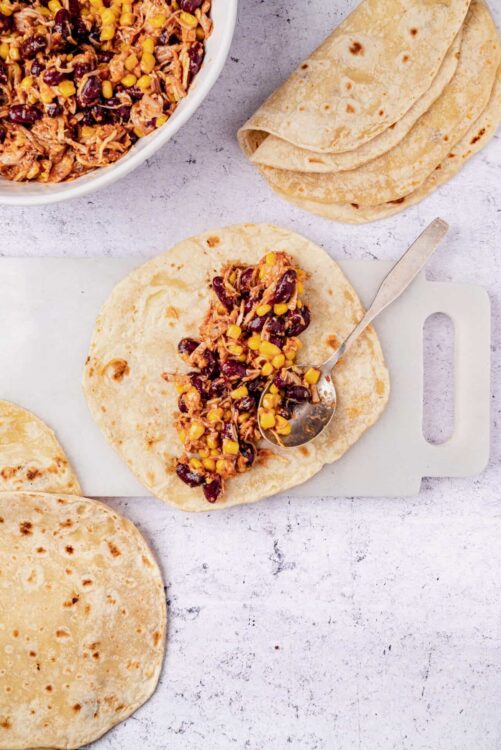 Savory bean and shredded chicken filling on flour tortillas for homemade burritos.