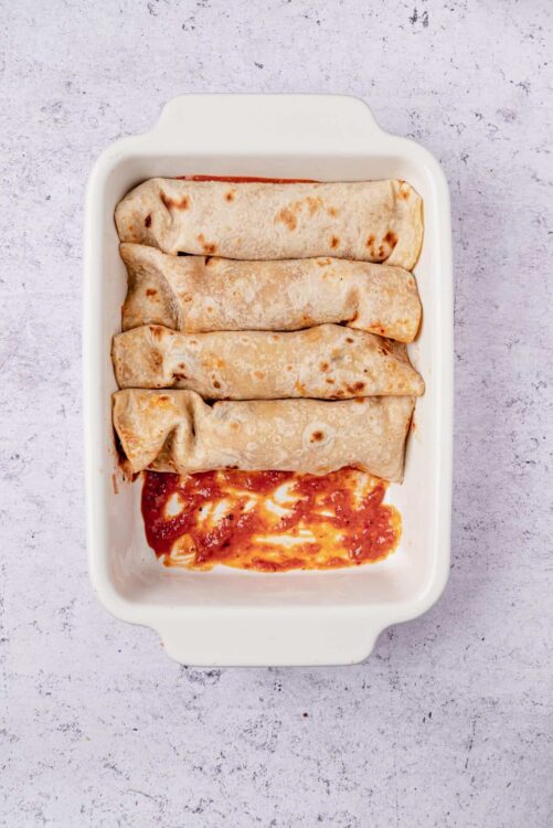 Stuffed enchiladas with melted cheese in a white baking dish, ready for baking.