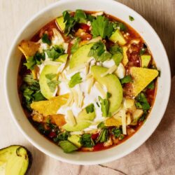 Creamy chicken tortilla soup garnished with avocado, cheese, and cilantro. Perfect for a cozy dinner.