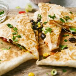 Creamy chicken and black bean quesadillas with melted cheese and fresh herbs on wooden cutting board.