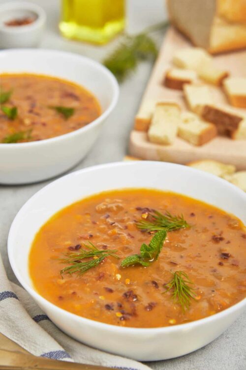Creamy tomato soup with herbs and bacon garnish, served in white bowls. Perfect comforting meal with bread slices and fresh herbs.